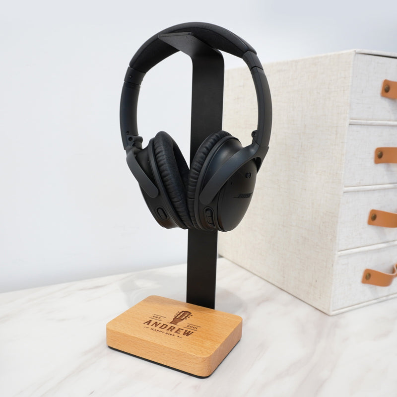 Personalised headphone stand engraved with a name, featuring a beech wood base and black aluminium holder.